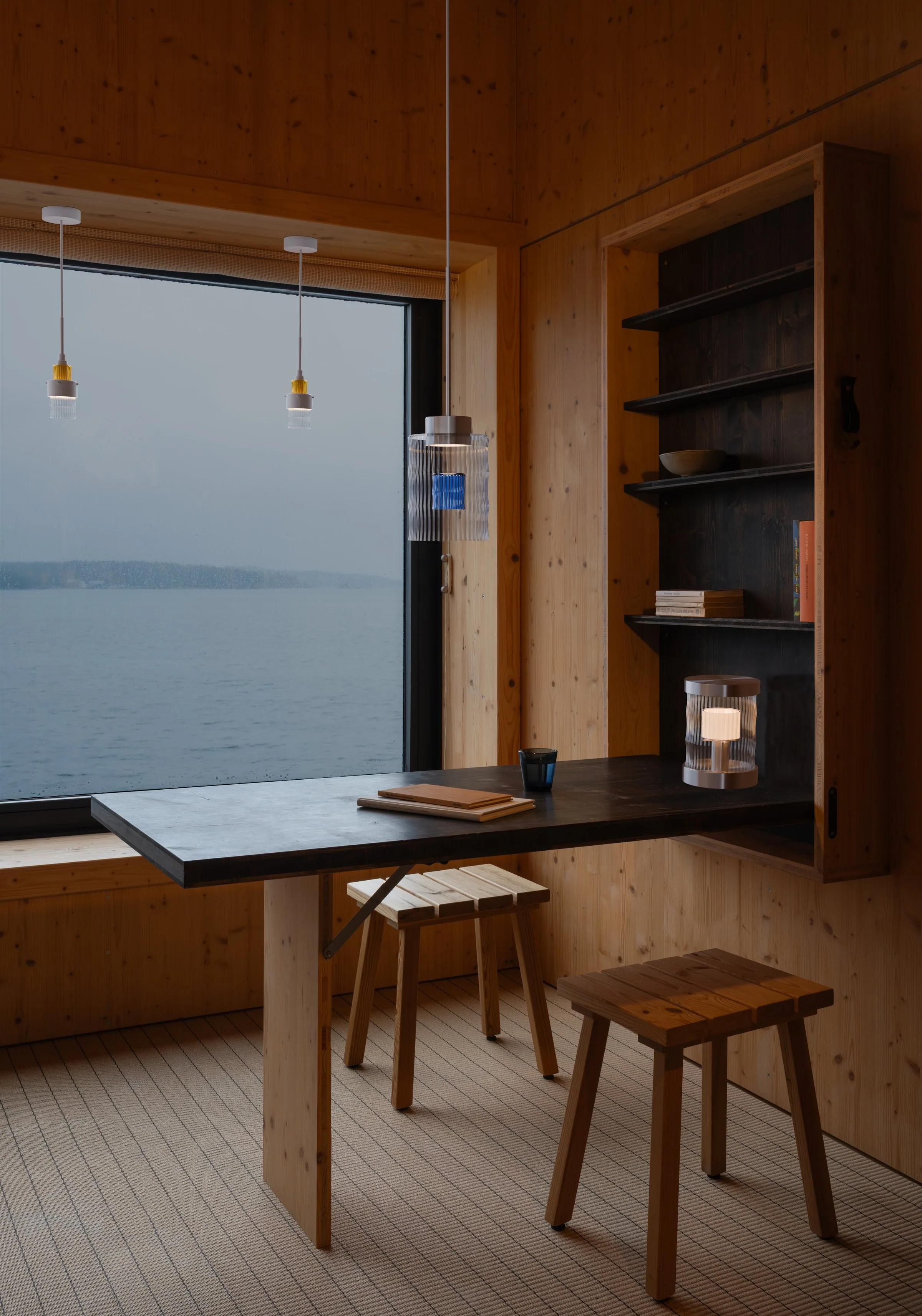 Rendering of a wooden room by the sea with Celina above the table and the family's other two lamps