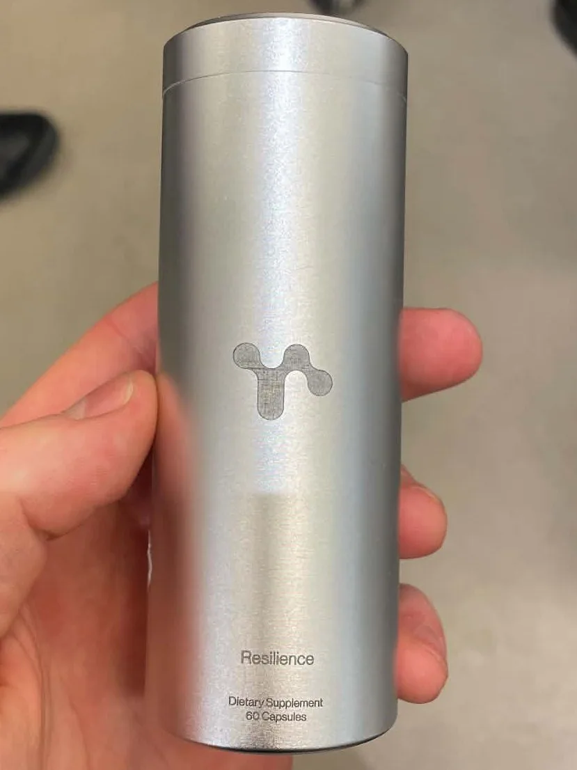 The real brushed aluminium tin held in a hand, with the symbol, the product name Resilience and the text Dietary Supplement, 60 Capsules